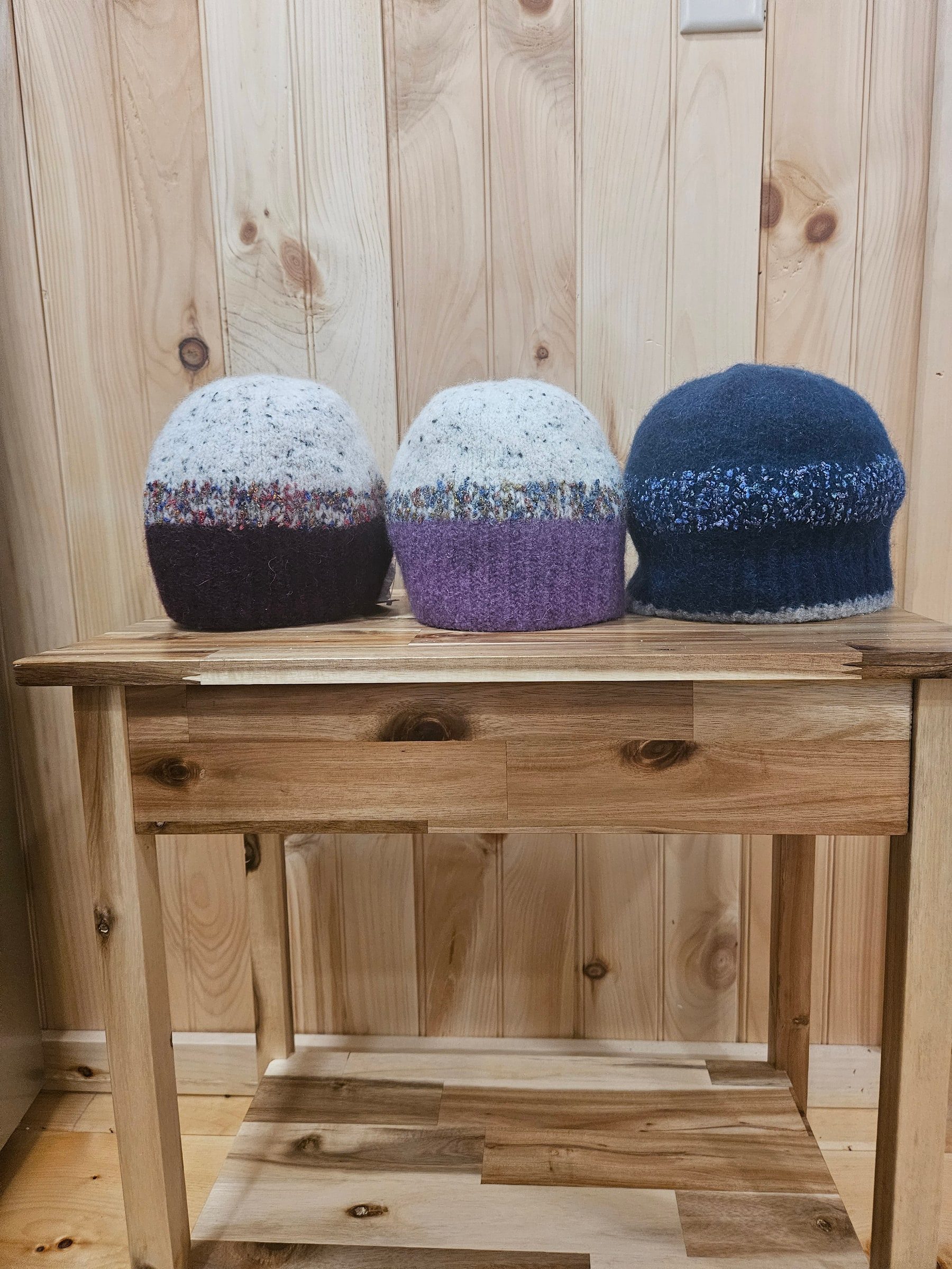 Three felted hats in burgundy, purple, and navy lined up on a wooden table.