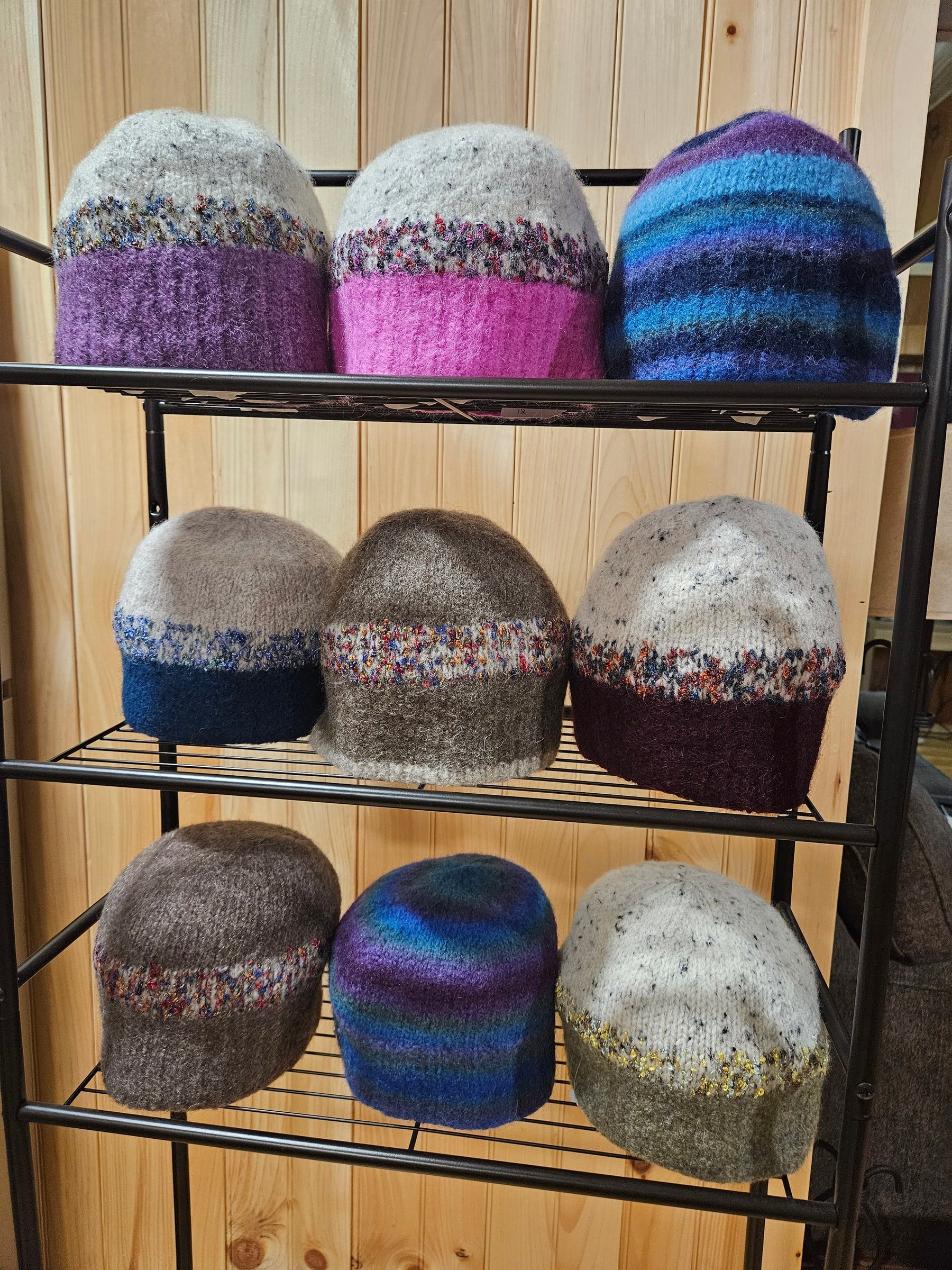 Close view of nine felted hats arranged on a three-tier black wire rack against a pine wall.